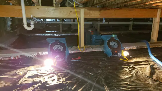 Drying fans and a work light on plastic sheeting inside a crawl space